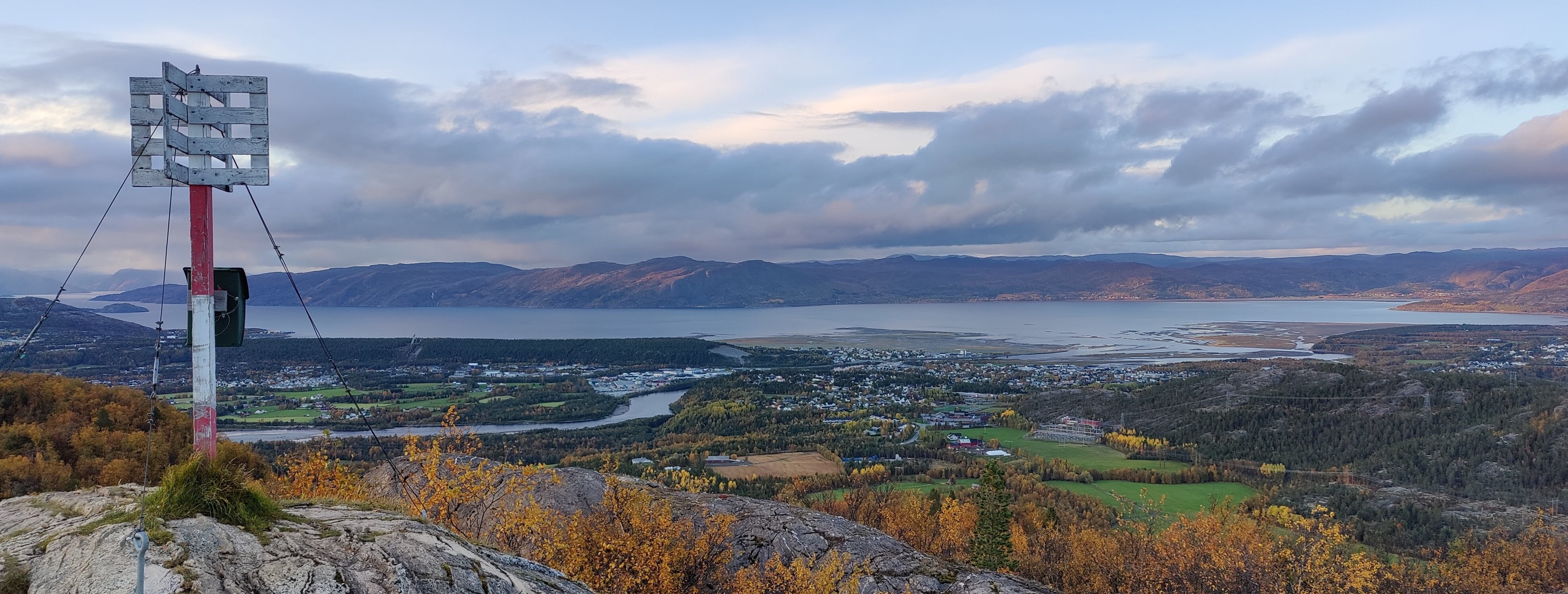 Vy från ett berg över en fjord och en by. En älv flyter genom byn och ut i fjorden. Träden har vackra höstfärger.